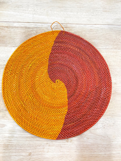 This mandala wall piece presents a yin-yang design, with a warm golden yellow on one side and a rich terracotta red on the other, both featuring intricate woven textures.