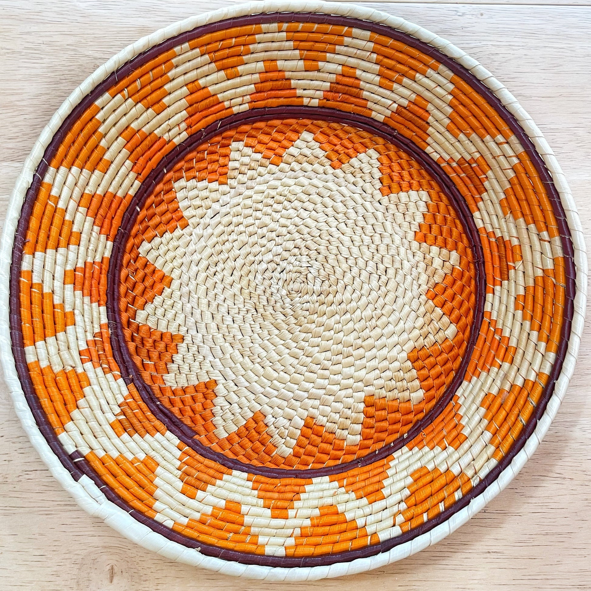 Handwoven from Amazonian tucuma palm fibers, this bowl showcases a captivating spiral pattern in natural, orange, cream, and dark brown.  A beautiful piece of craftsmanship for fruit or home decor