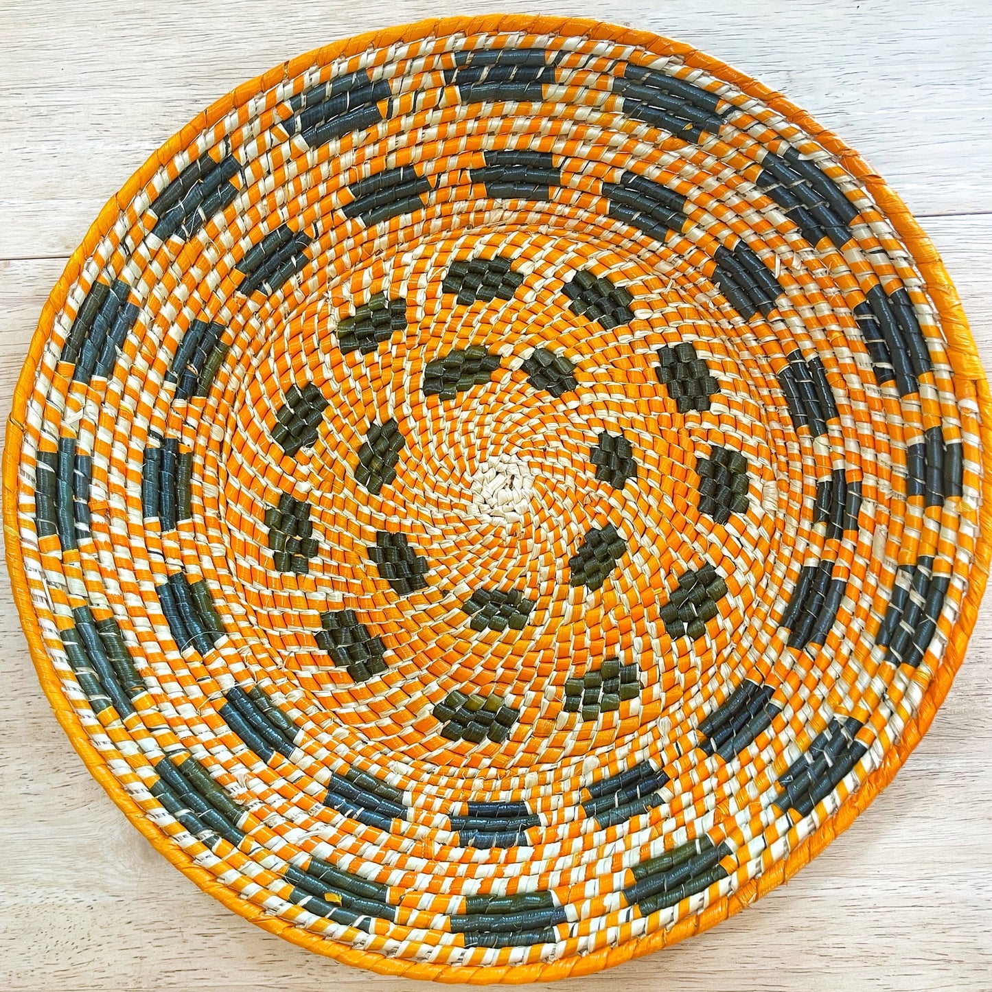 A large, handwoven Amazonian bowl crafted from tucuma palm fibers, displaying an intricate spiral pattern. The design features concentric circles in shades of orange, green, and black, highlighting the artistry of Amazonian weaving techniques