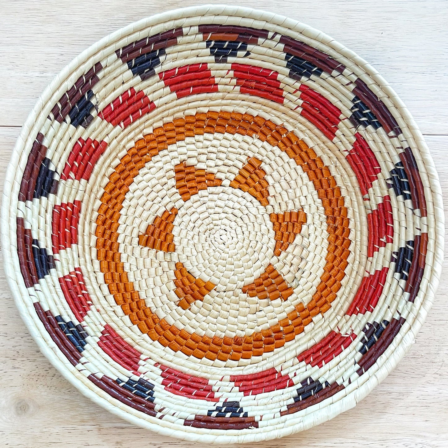 Handwoven tucuma palm fiber basket features a swirling pattern in natural, red, dark blue, and various shades of brown. Showcasing traditional Amazonian craftsmanship, it serves as a fruit basket or decorative piece. 