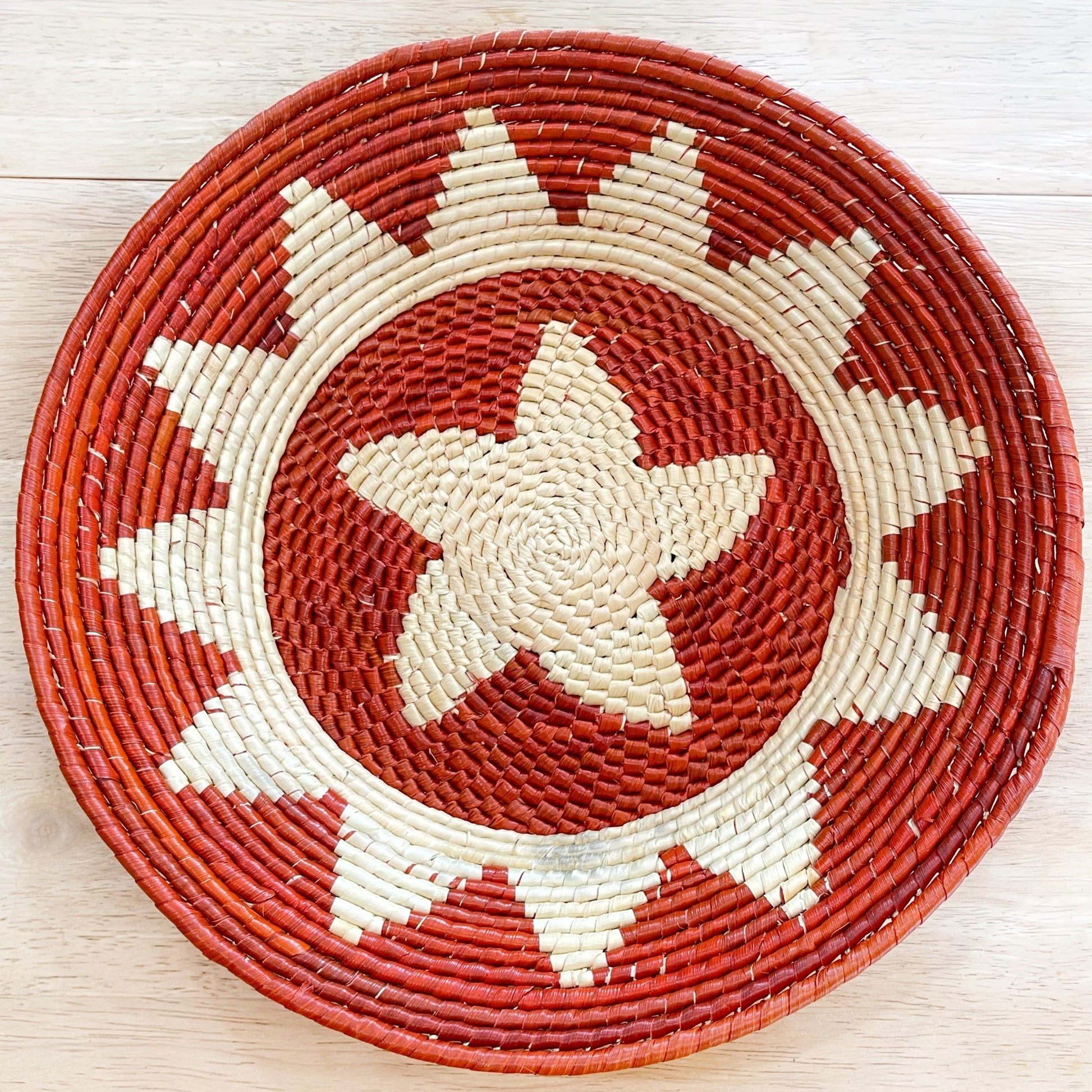 Handwoven Amazonian bowl made from tucuma palm fibers. Features a geometric zigzag pattern in shades of brown and natural fiber with red accents. 