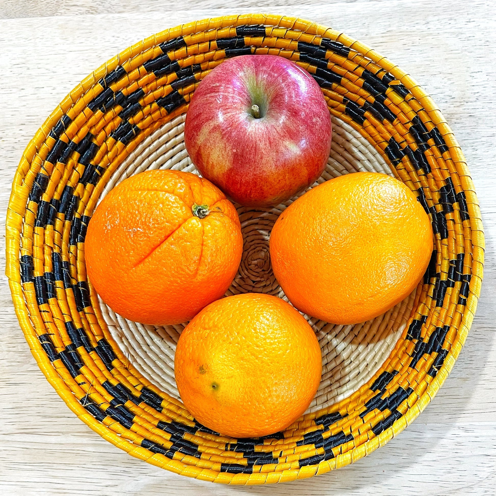 Woven Tucuma palm bowl cradling an apple and oranges, illustrating its use and the striking black and orange weave pattern.