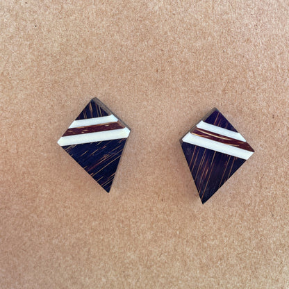 The image shows a pair of handcrafted, diamond-shaped earrings made from recycled bone, set against a brown background. The intricate design features natural brown hues with white inlay stripes, and they have 925 sterling silver backings, blending traditional materials with precious metals.