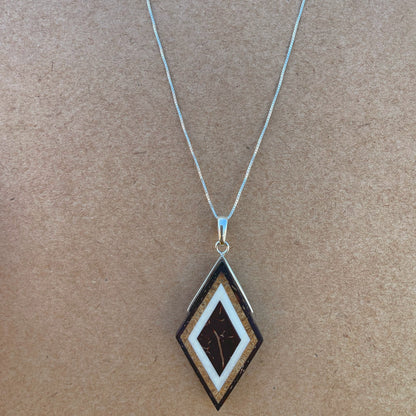 Handcrafted silver pendant in a diamond shape. Intricate layers of babassu & coconut seed inlays showcase artistry and natural materials.