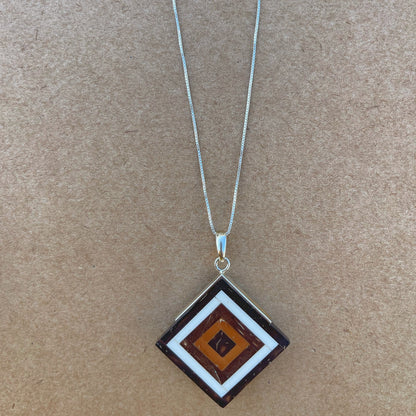 Square-shaped silver pendant with concentric geometric seed marquetry, utilizing repurposed Amazonian babassu and coconut seeds. The pendant features a natural color palette, with the deep browns of the seeds set against the silver frame, creating an earthy yet elegant aesthetic.