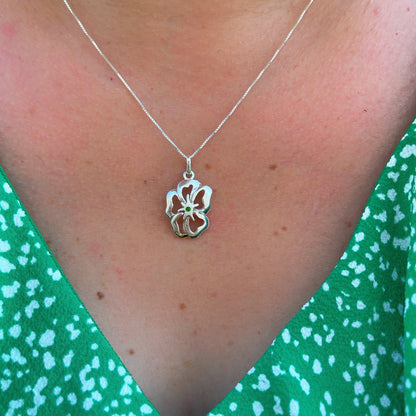 A silver flower pendant with a green malachite inlay on a necklace, set against a green patterned fabric, evoking a fresh, natural aesthetic.