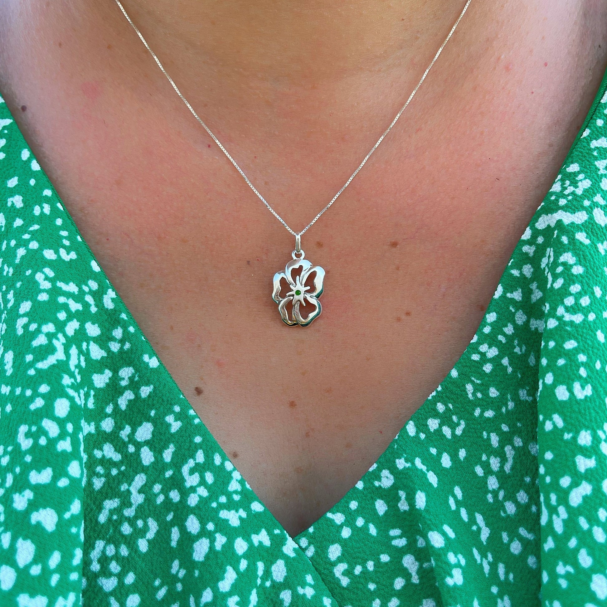 Silver flower pendant with a green malachite heart rests on a bed of patterned green fabric, evoking a sense of springtime freshness.