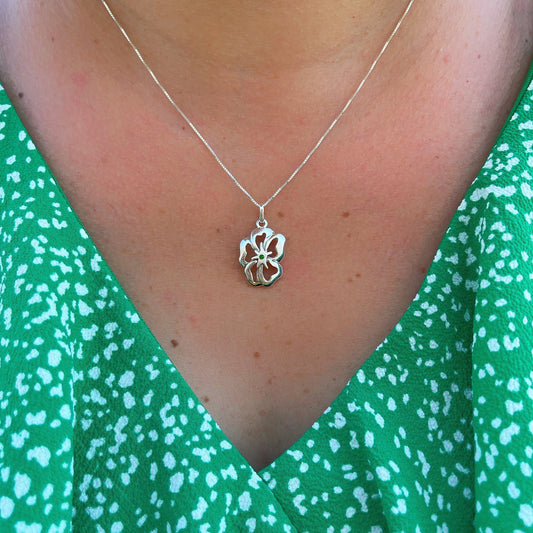 Silver flower pendant with a green malachite heart rests on a bed of patterned green fabric, evoking a sense of springtime freshness.