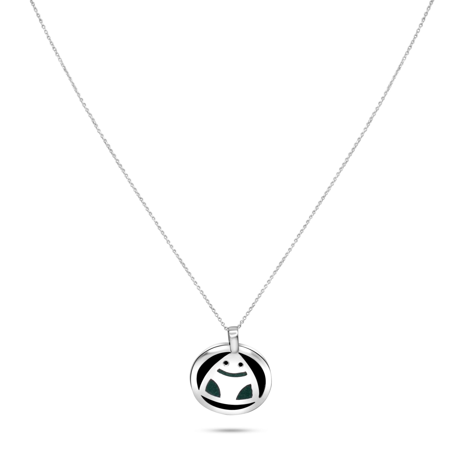 The image presents a silver necklace with a round pendant featuring a stylized frog design. The pendant is crafted from .925 sterling silver and showcases sections of dark coconut shell, complemented by rich green malachite inlays that form the frog’s limbs. The design is inspired by Amazonian culture, symbolizing nature's vitality. The pendant hangs from a silver link chain and offers a harmonious blend of natural materials and cultural imagery.