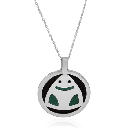 This image displays a circular .925 sterling silver necklace featuring a stylized Muiraquitã frog pendant. Made with coconut shell and green inlay, the pendant embodies Amazonian cultural motifs and the essence of nature.