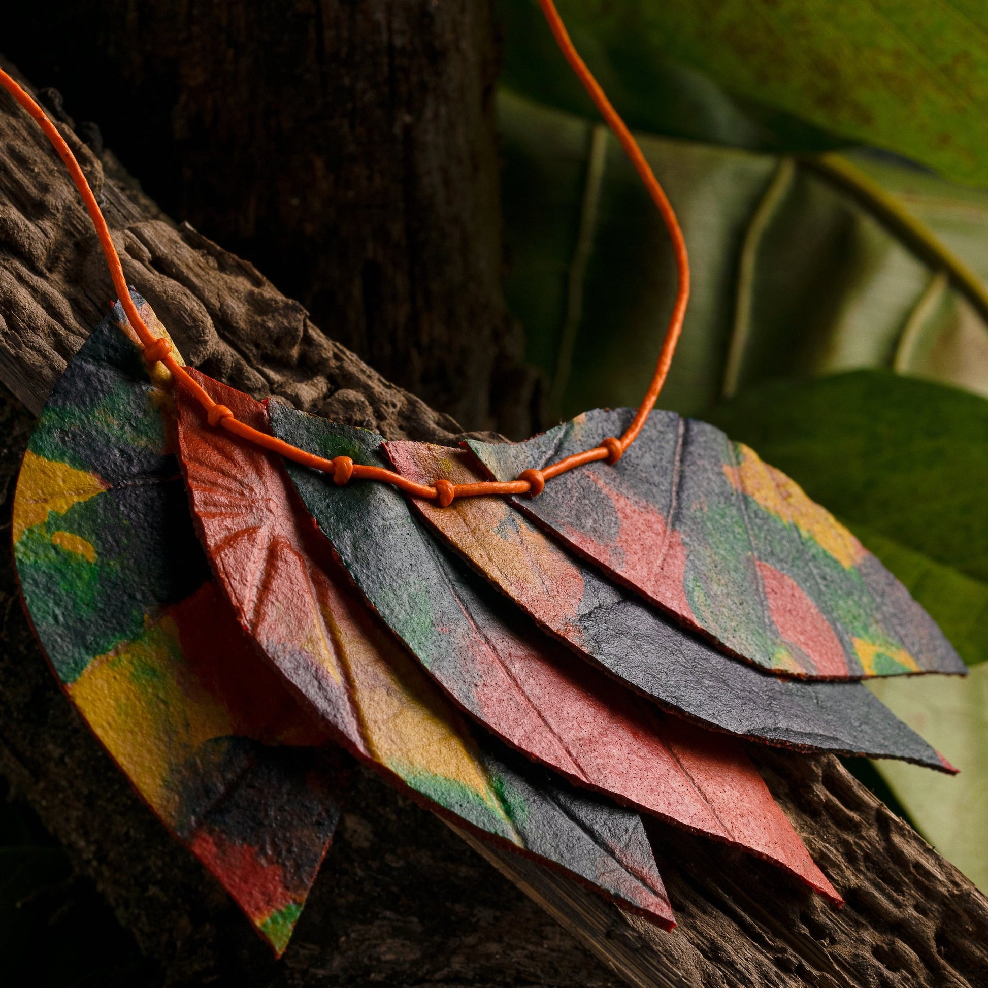 A close-up photo of a handcrafted necklace made from natural rubber and açaí seeds. The necklace has colorful leaf-shaped pendants.