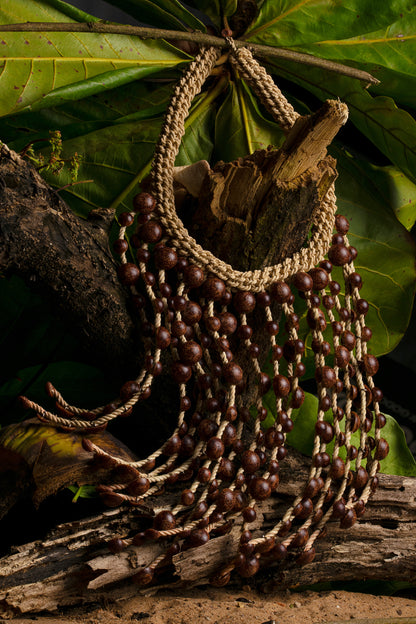 A handcrafted necklace with dark brown açai seeds and beige fibers rests against a natural backdrop, embodying a rustic and organic aesthetic.