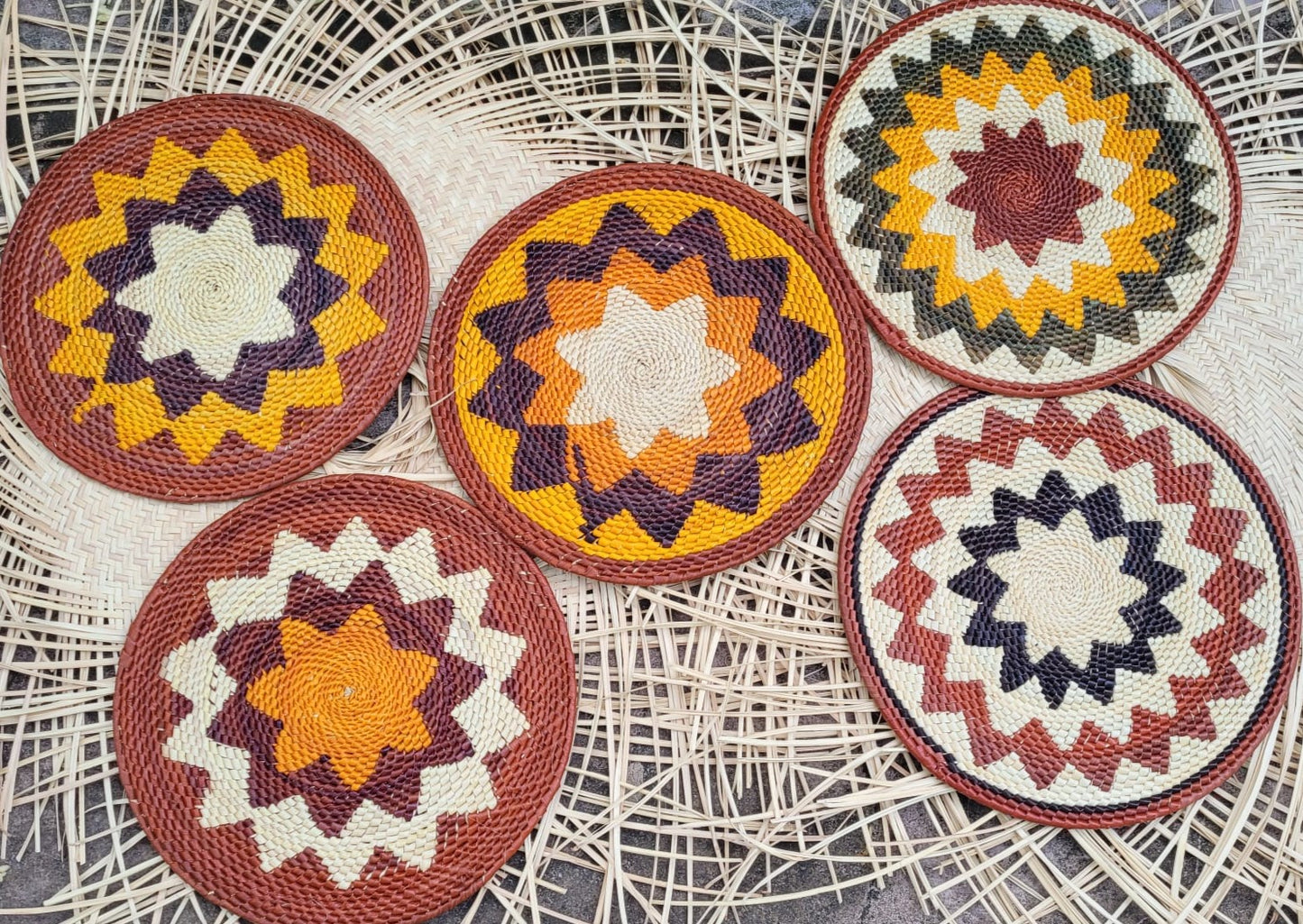 Four round placemats with starburst patterns in navy, orange, cream, and brown are arranged on a lace doily.