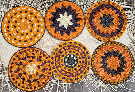 Six round placemats feature geometric designs in shades of orange, black, purple, and white on a lacy background.