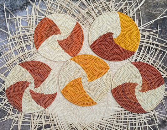 Five round woven trivets featuring a dynamic swirling design in cream, yellow, and two shades of brown set against a woven wicker background