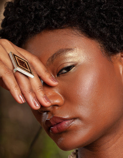 A close-up of a model showcases a .925 sterling silver ring with an elongated hexagonal shape, adorned with seed marquetry, babassu, Brazil nut husk, and coconut.