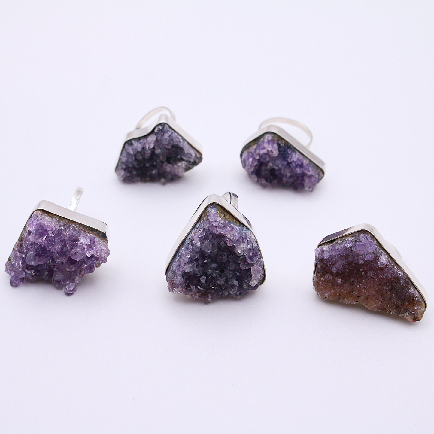 Five raw amethyst rings, handcrafted in sterling silver, lie on a white background displaying the natural material's patterns.