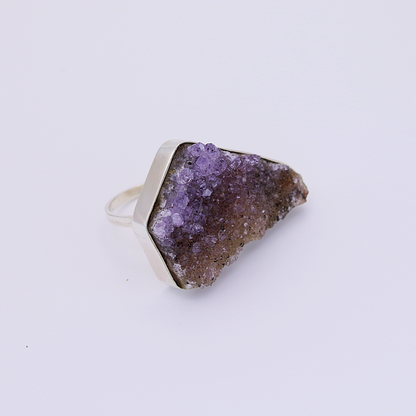 A single, organic-shaped raw amethyst ring sits on a white background.