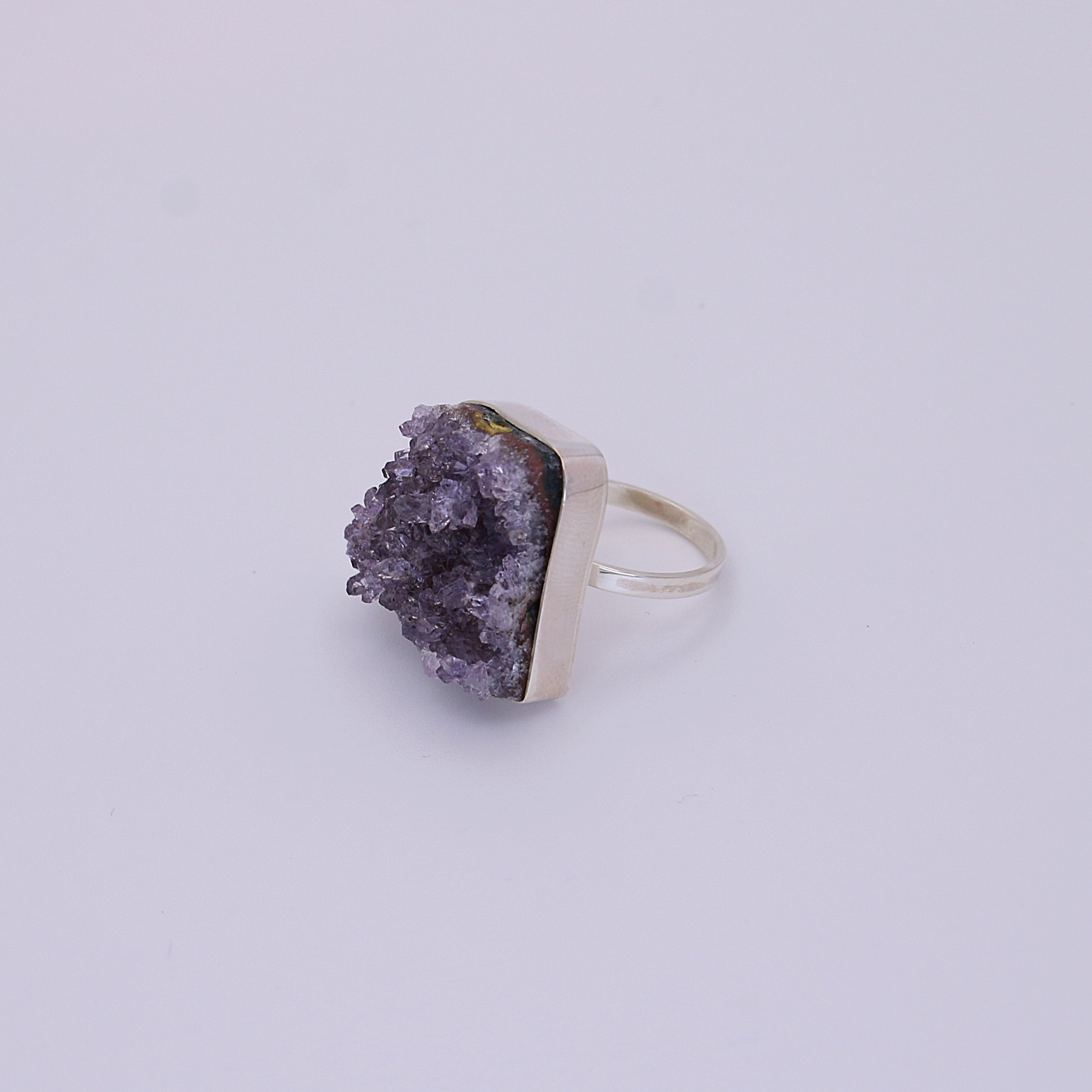 A one-of-a-kind raw amethyst ring with unique patterns lies on a pristine white background.