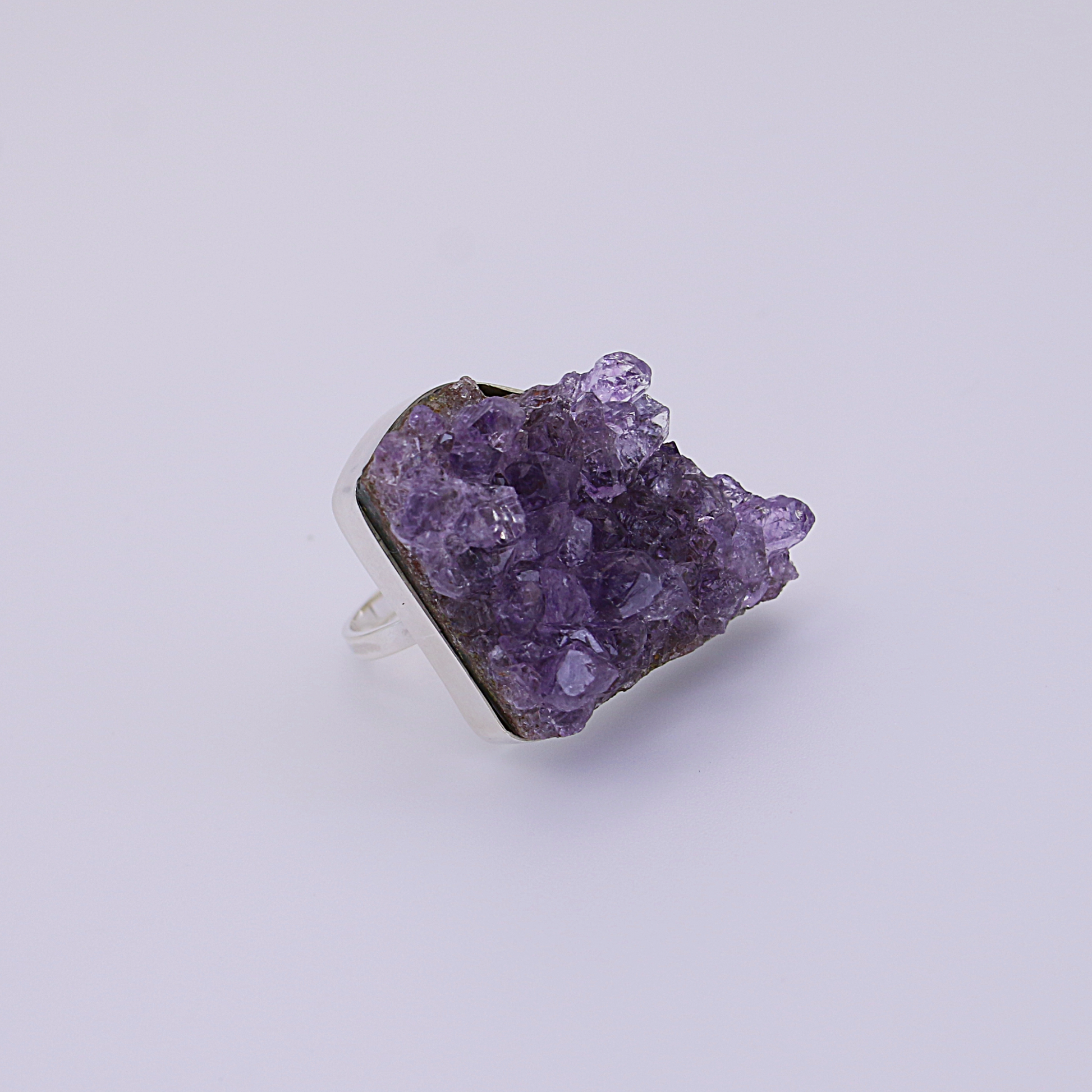 A solitary raw amethyst ring with a hint of sparkle rests on a stark white background.