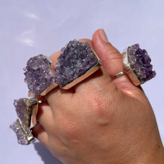  A hand showcasing five stunning raw amethyst rings, one on each finger.