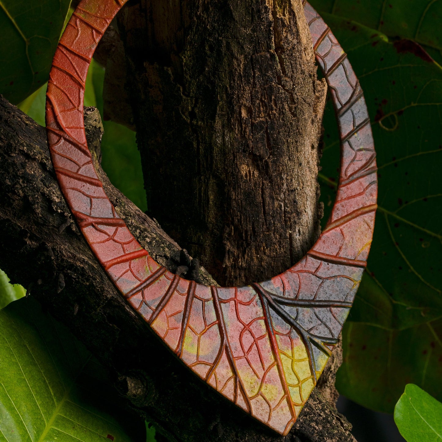 Bold 'Shield' necklace crafted from Amazonian rubber, featuring a spectrum of red to yellow hues with a leaf vein pattern, evoking the essence of the rainforest