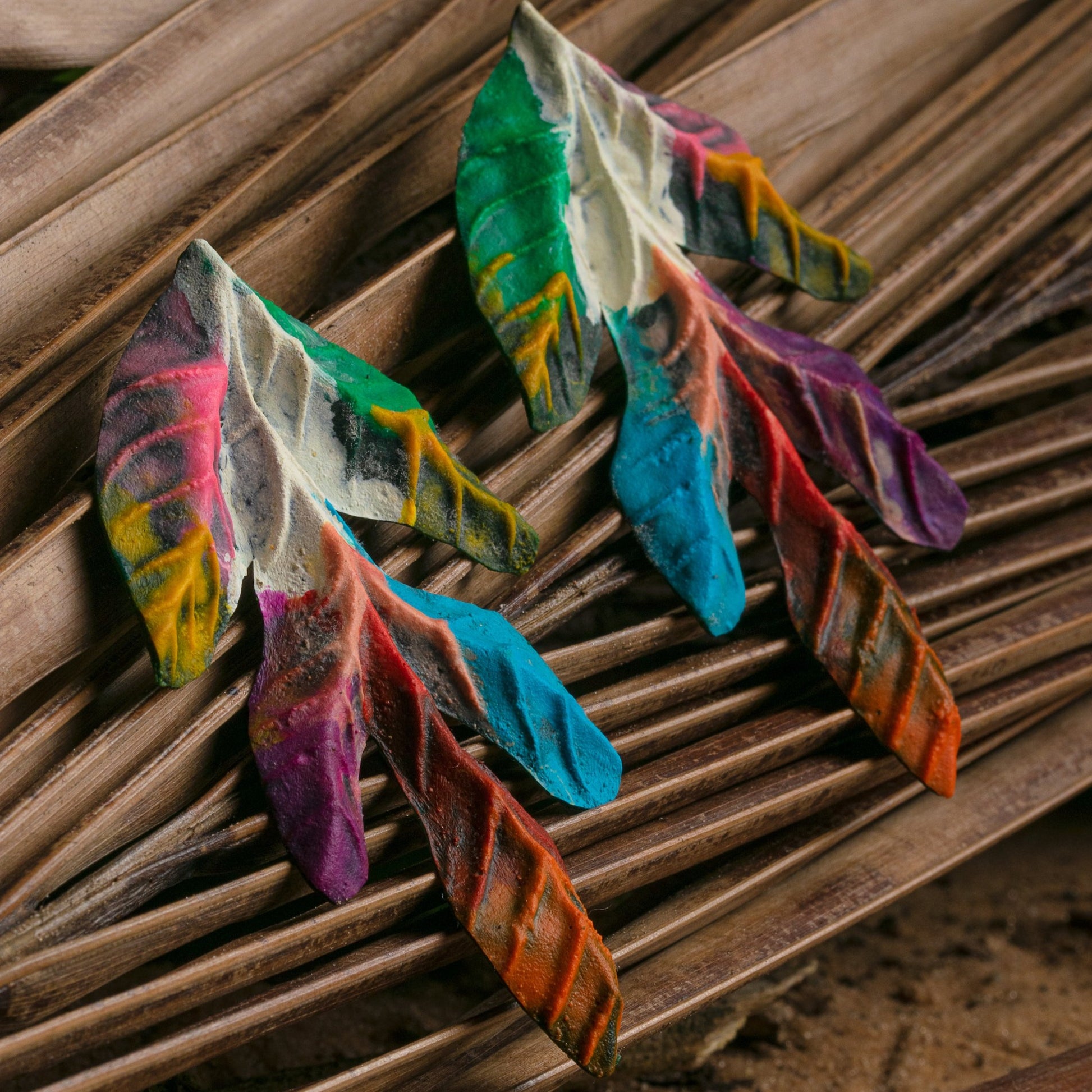 Colorful, leaf-shaped artisan earrings on fiber mat, made from sustainable latex and açaí, featuring a vivid, natural vein pattern.