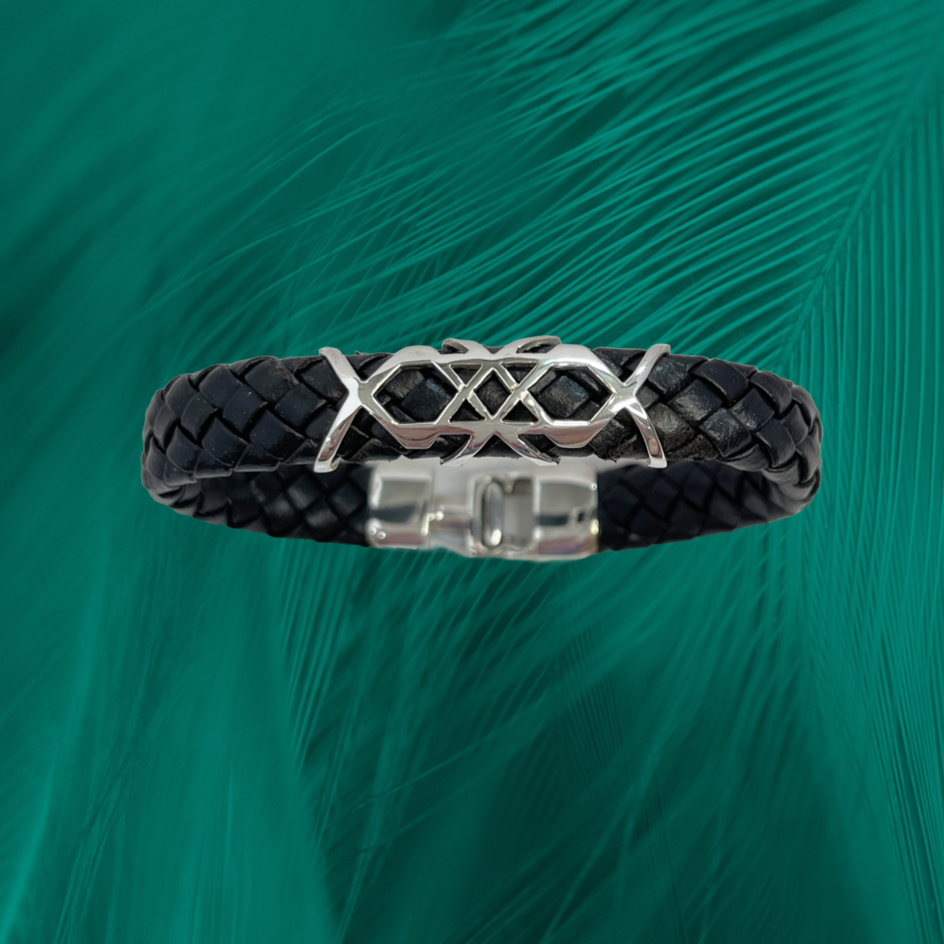 Sleek bracelet with silver wave-inspired motif, contrasted by black vegan leather, complete with a polished clasp on a green feathered canvas.