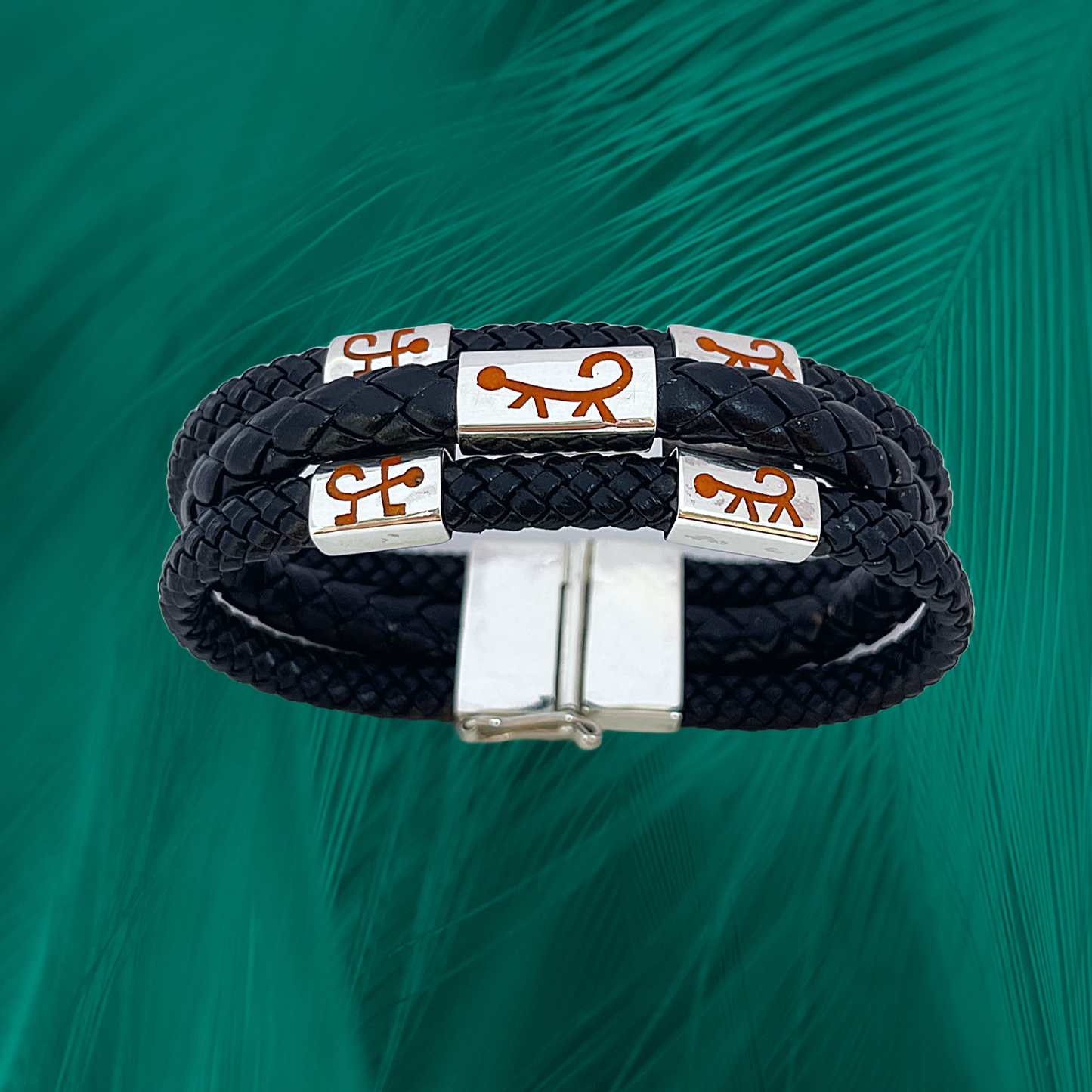 This is a bracelet featuring a triple strand of black vegan leather, accented with .925 silver charms depicting Marajoara monkey designs, fastened by a silver clasp.