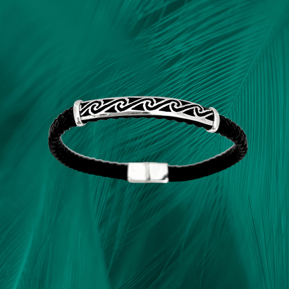 Sterling silver bracelet featuring a Pororoca wave pattern. Polished wave design against a braided black leather band with a sleek silver clasp. Set against a textured emerald backdrop.