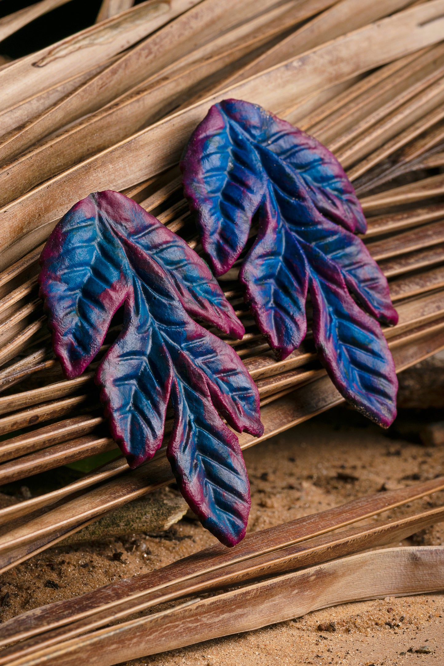 Artisan-crafted, blue and purple leaf-shaped earrings on natural mat, made from rubber latex and açaí fibers.