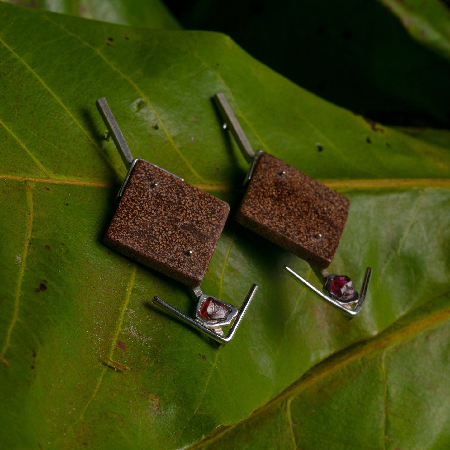 Handcrafted .925 silver earrings, each with a square amethyst, set on bases of recycled açaí and peach palm, resting on a vibrant leaf.