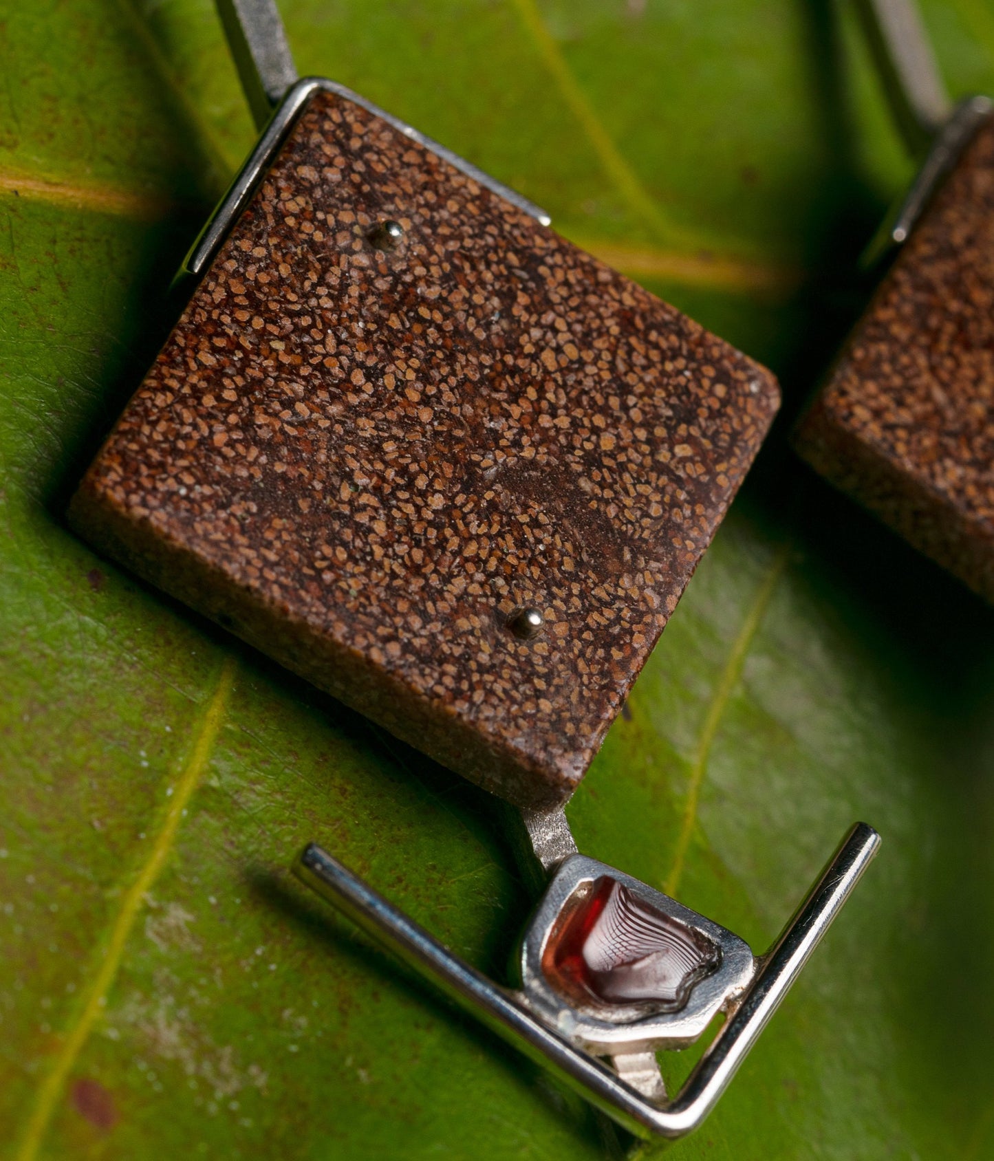 Close-up of silver earrings with amethyst and textured recycled açaí and peach palm inlay, artfully placed on a green leaf