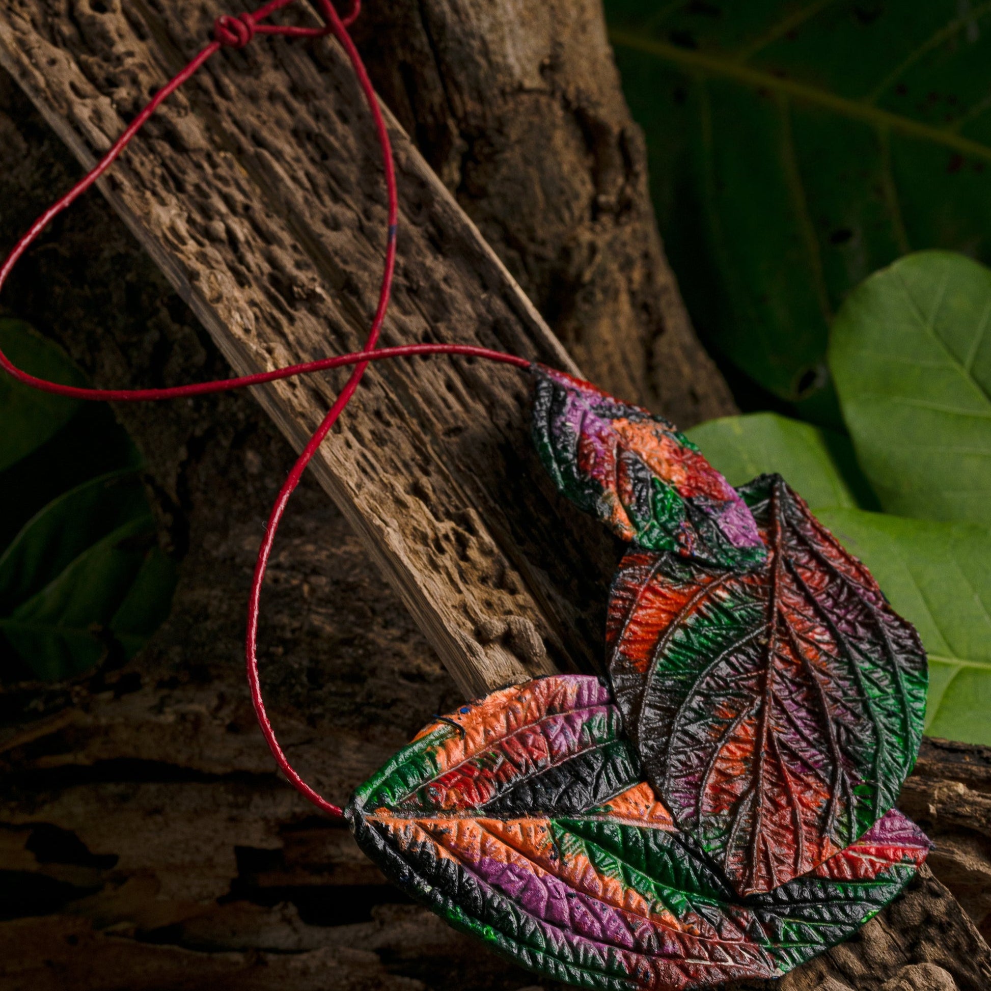 Handcrafted leaf necklace bursts with fiery colors! Natural rubber & açaí seed fibers create intricate details. Bold red cord contrasts with the vibrant purple-black, orange, red & green design.