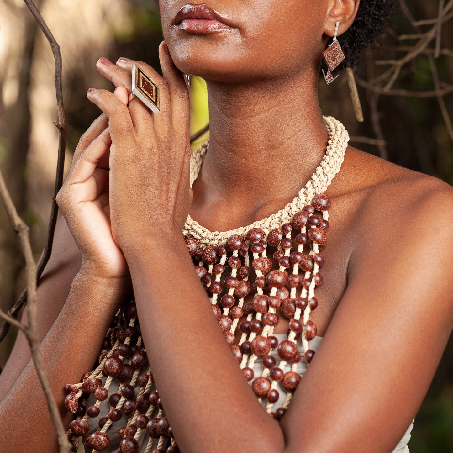 A woman adorned with earth-toned jewelry: a multistrand necklace of glossy açai seeds, a fiber-woven choker, geometric resin earrings, and a ring, all showcasing natural Amazonian materials.