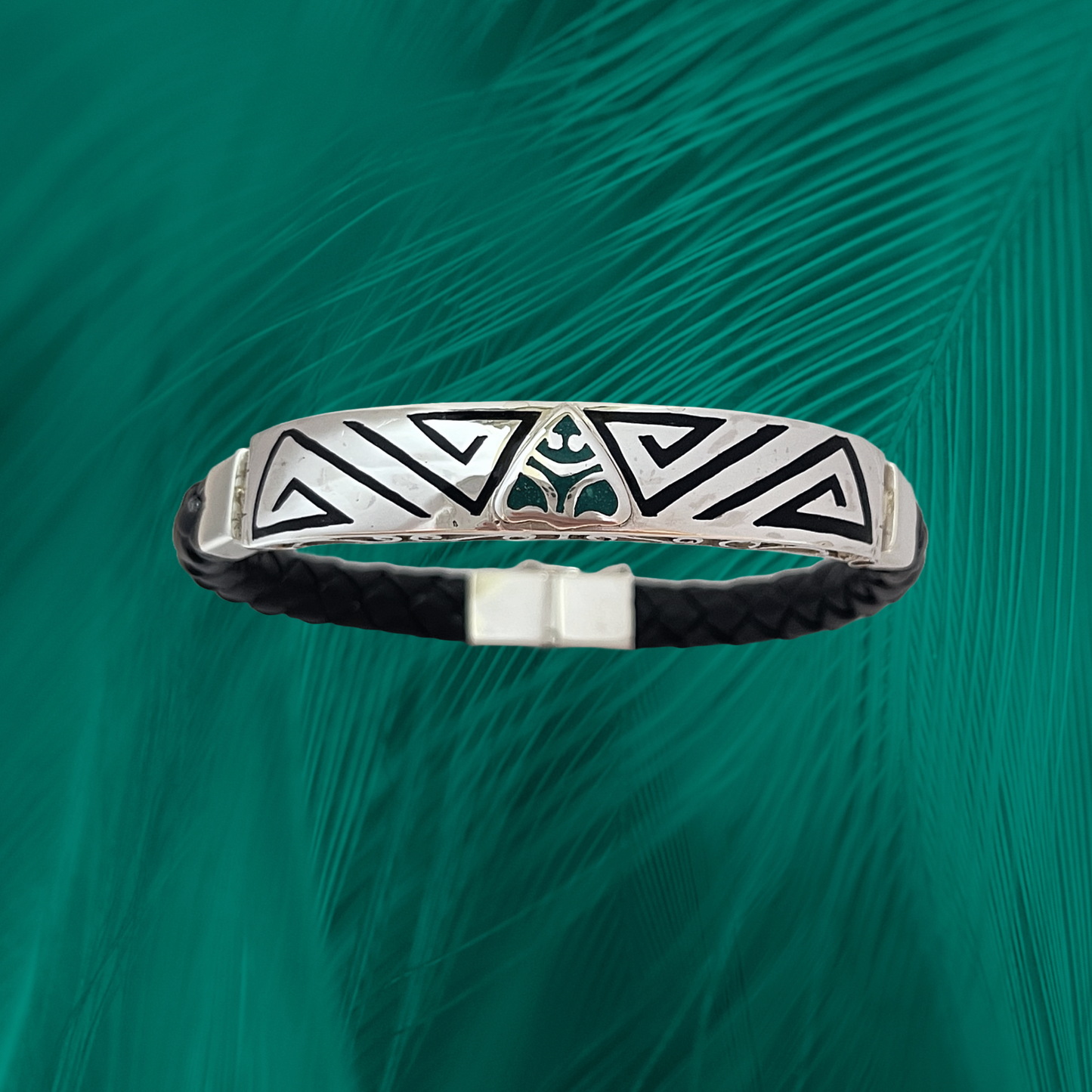 Sterling silver Muiraquita bracelet on a vegan leather strap, set against a green feather-like background. It features tribal patterns and a mythical spirit animal symbol, embodying a connection to the Amazon rainforest.