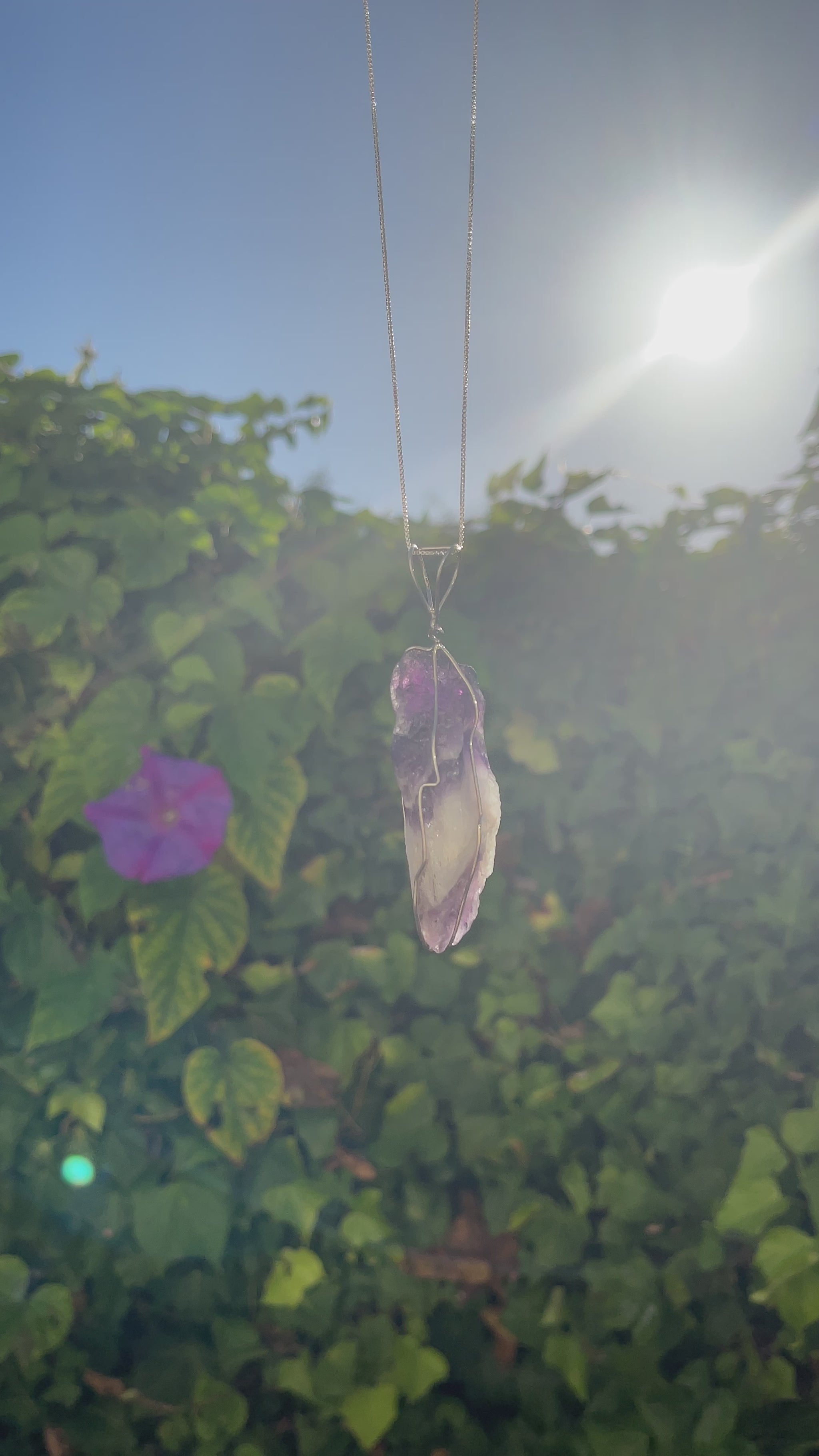 An uncut amethyst gemstone pendant, its violet tones fading into white, suspended by a whimsical heart-crafted silver wire.