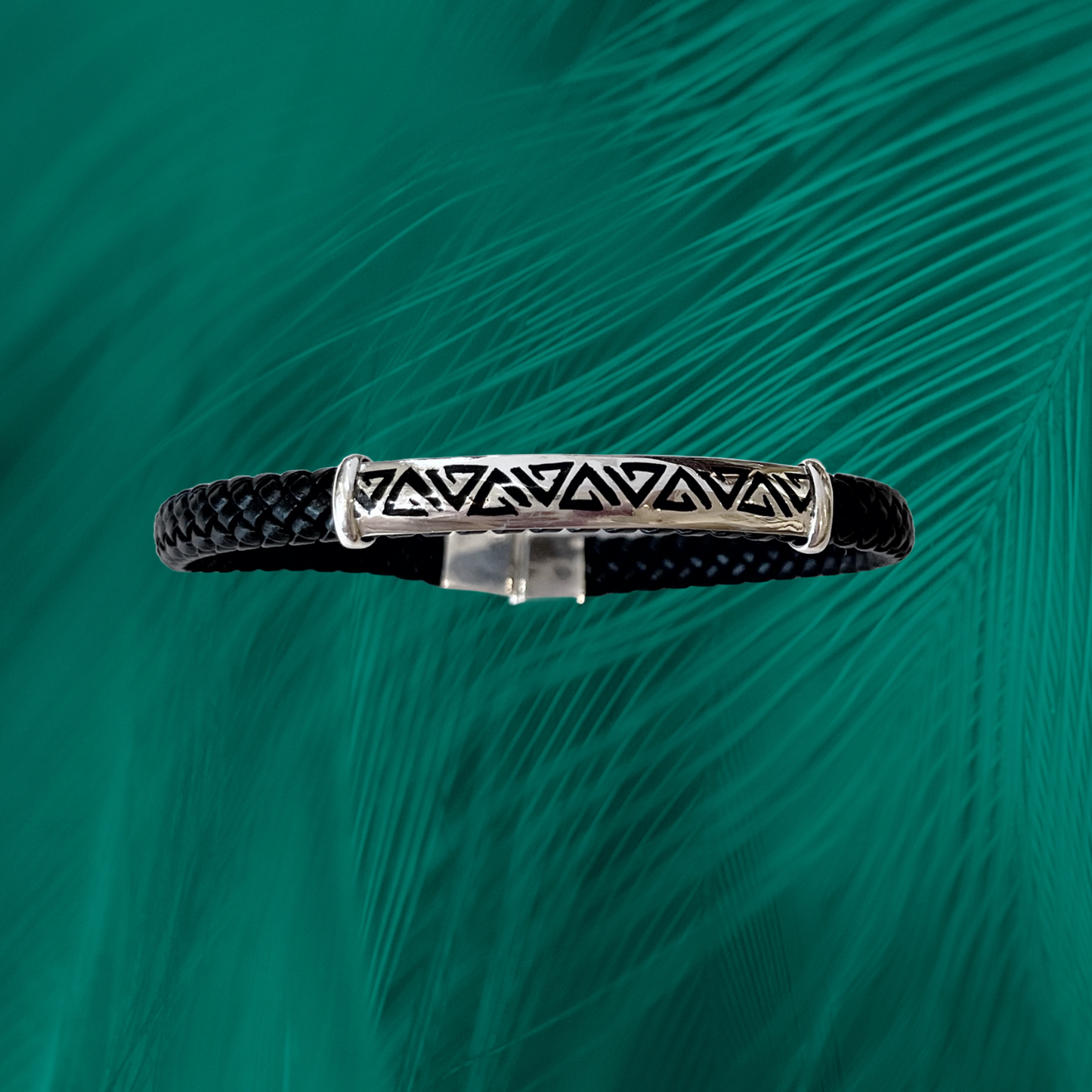 A Brazilian-crafted .950 silver bracelet with an Amazon-inspired triangle pattern on a braided vegan leather strap set against a green backdrop.