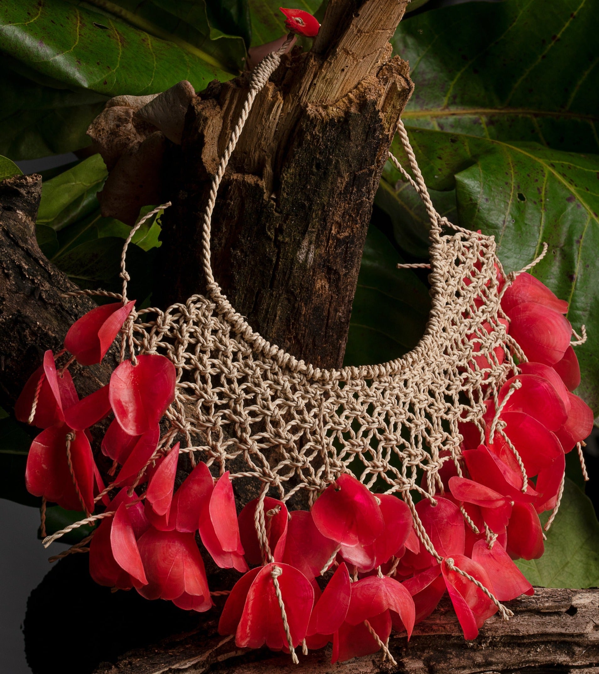 The necklace features miriti fiber and upcycled red “Escama de Pirapema” fish scales, handcrafted by fishermen's wives, transforming waste into an enchanting adornment.