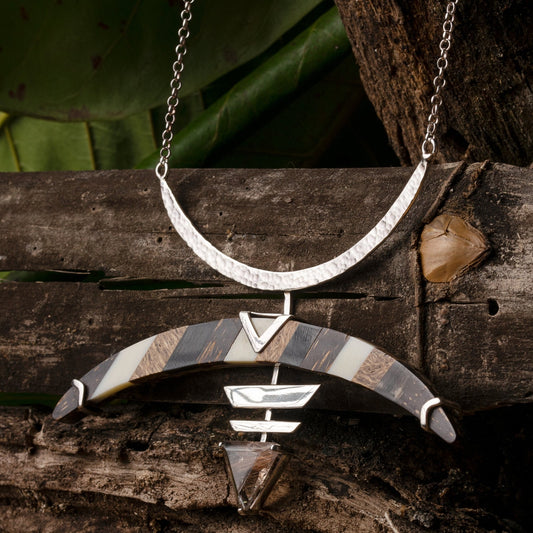 Sterling silver Bow & Arrow necklace. Inspired by Amazonian tradition, it features a marquetry base made from recycled seed pods & bone. A quartz gemstone completes the arrowhead design