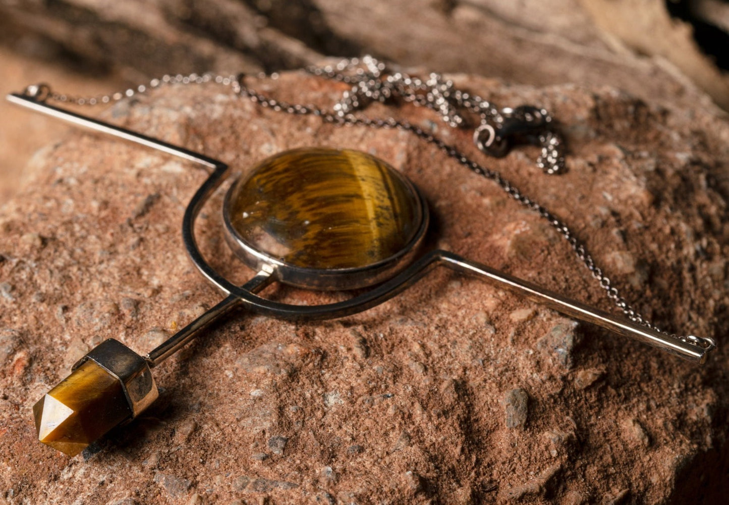 A .925 sterling silver necklace with a lustrous tiger's eye stone, laid on stone, combining natural beauty with artisanal skill.