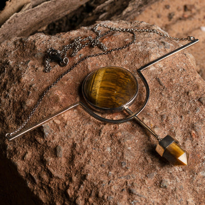 Sterling silver necklace with a circular tiger's eye stone and a geometric pendant on a rock surface, evoking earthy elegance