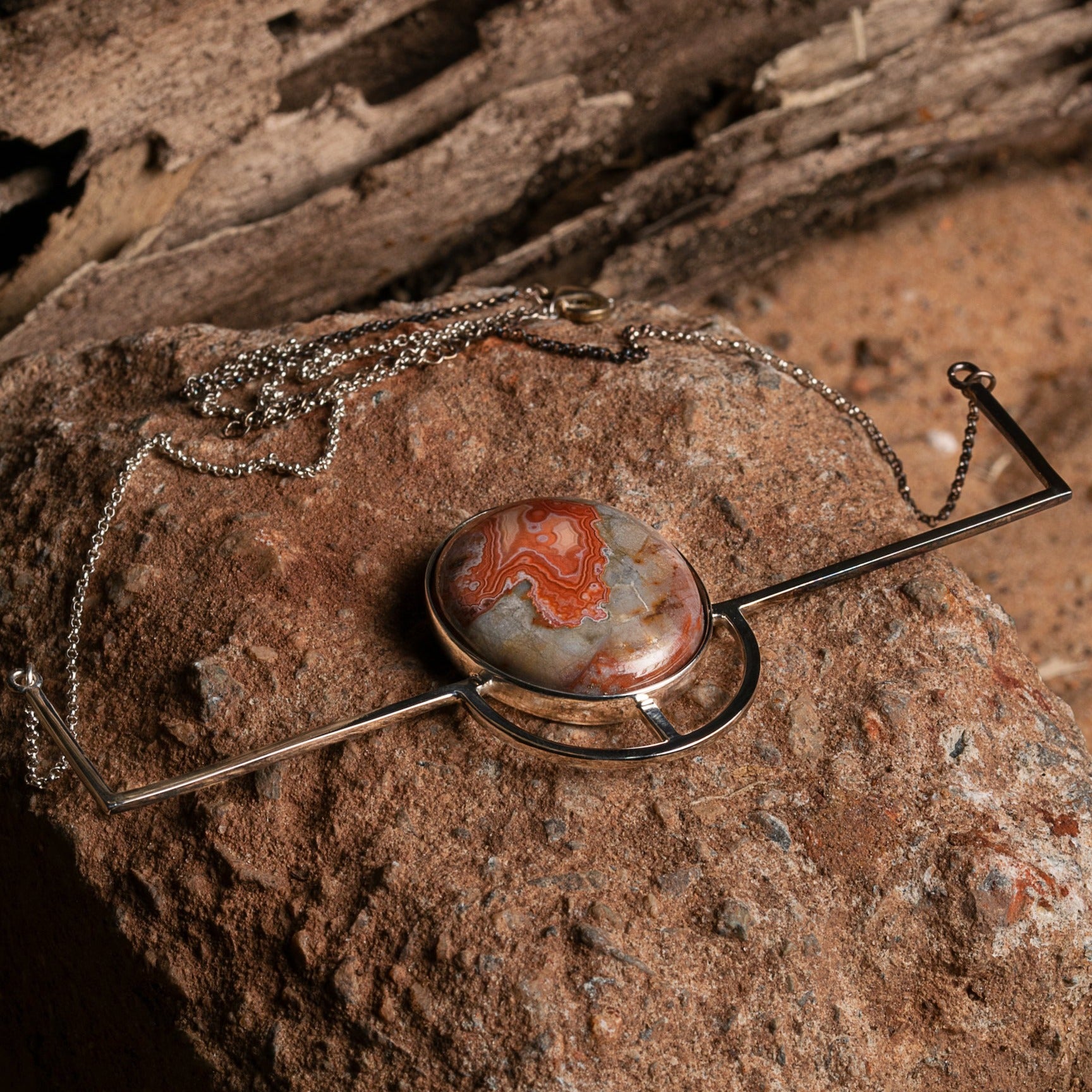 A sterling silver necklace with an intricate crazy lace agate pendant, displayed on a rock.