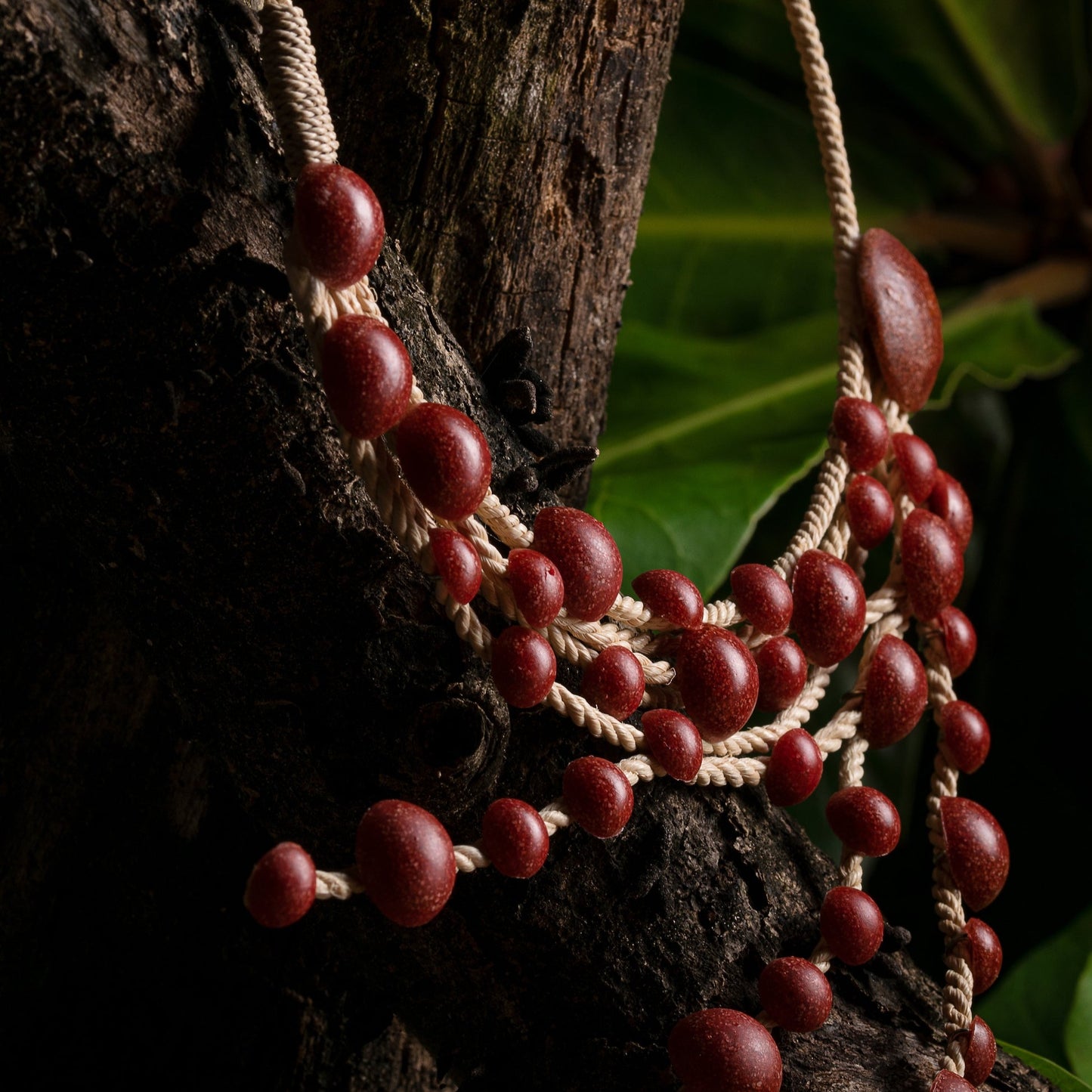 Side of the necklace showing the details of a red handcrafted necklace with Açaí seeds and Buriti fiber against a natural backdrop. This necklace is 100% sustainable.