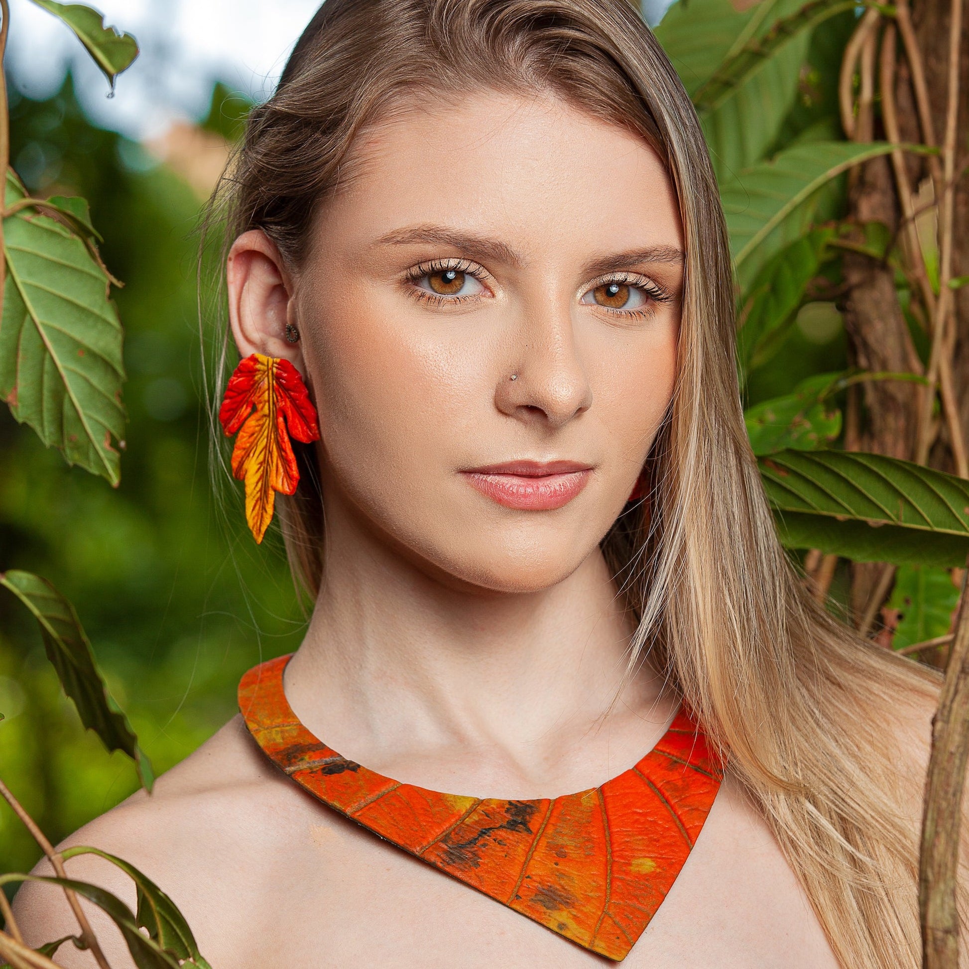 Model showcasing a 'Shield' necklace, handcrafted from natural Amazonian rubber with vibrant orange and red açaí seed fibers, creating a bold statement piece