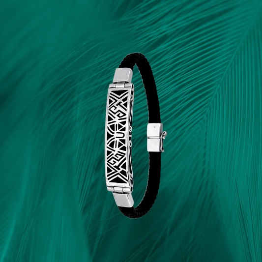 A 950 sterling silver bracelet with intricate geometric patterns, paired with a black premium vegan leather band, against a teal feather backdrop.