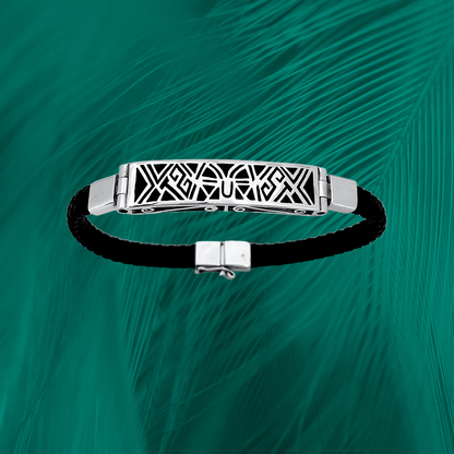 sterling silver bracelet with an elegant tribal inlay design on a black vegan leather strap, set against a vibrant green feathered texture.