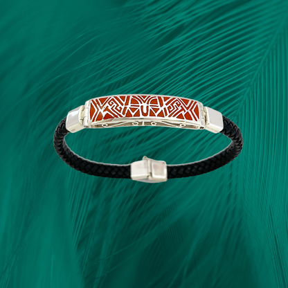 Sterling silver bracelet with red tribal patterns on an inlay, paired with a textured black vegan leather band, set against a green feather backdrop.