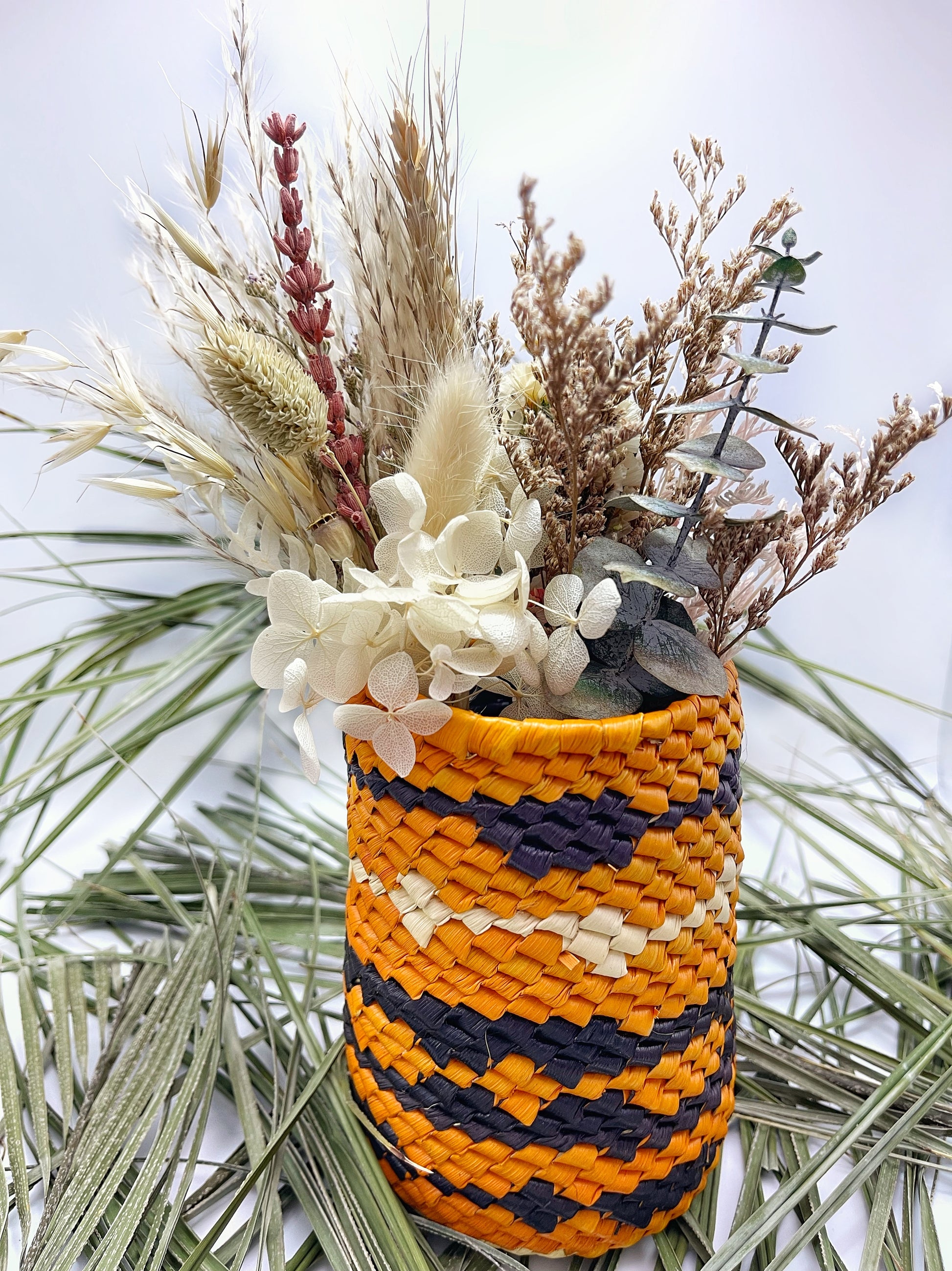 Vibrant orange and black woven holder filled with dried flowers, showcasing the holder’s versatile and decorative use.